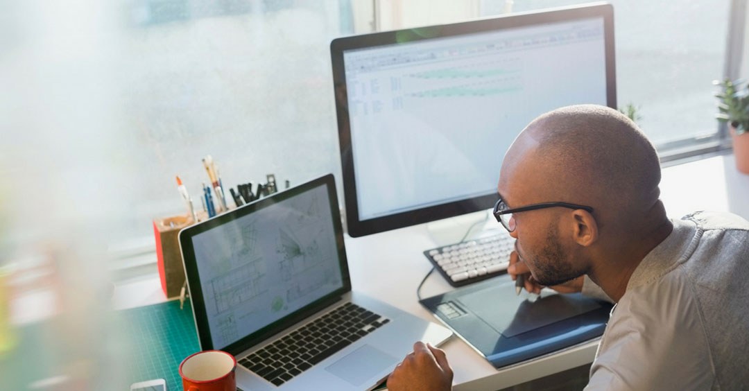 Man with glasses looking at laptop and monitors