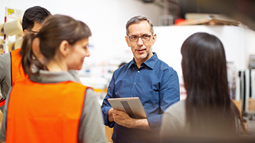 A man with a tablet converses with warehouse workers